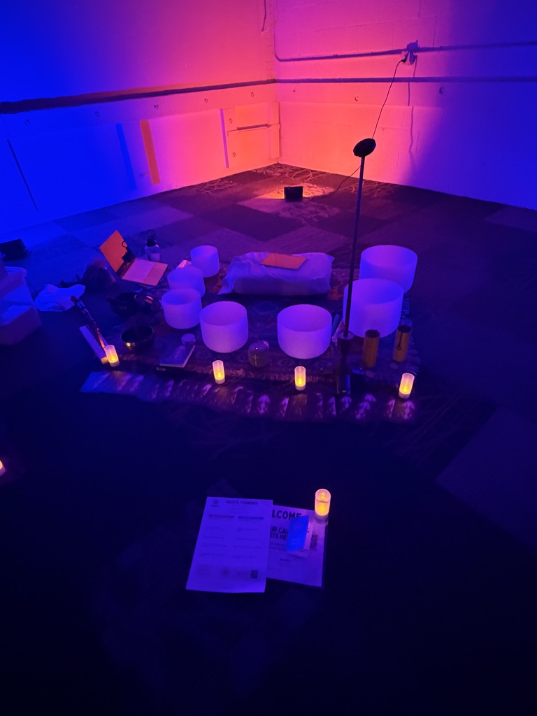 Crystal singing bowls and chimes arranged on a patterned rug inside COLAB Studio in Uptown Charlotte, lit in blue and pink for a sound bath