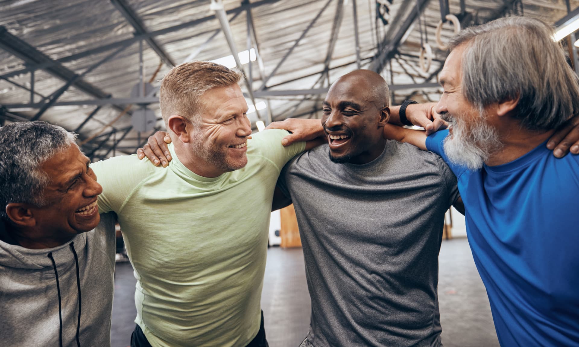 Men in a close circle with arms over each other’s shoulders, laughing indoors